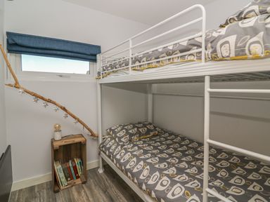 A small bedroom with a white metal bunk bed and a wooden crate bookshelf with books and a lamp at Haka Lodge in Devil's Bridge
