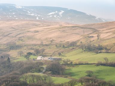 A rural farm with buildings surrounded by green fields and hills with patches of snow at Haka Lodge in Devil's Bridge