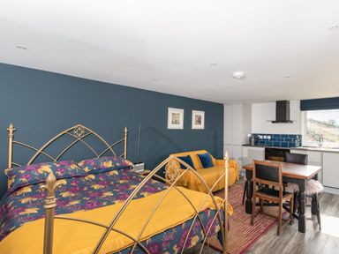 A bedroom with a bed floral bedding a yellow throw a yellow sofa with blue cushions a dining table with chairs and a kitchen area at Haka Lodge in Devil's Bridge