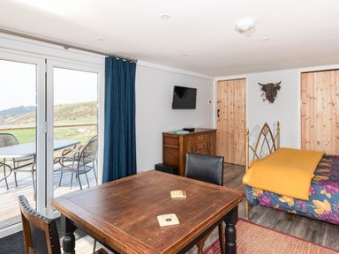 A room with wooden table and chairs a bed with floral bedding and a yellow blanket a wooden cabinet and sliding glass doors leading to an outdoor patio at Haka Lodge in Devil's Bridge
