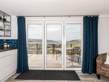 A kitchen area with a glass door leading to a deck with a table and chairs and a landscape visible outside at Haka Lodge in Devil's Bridge