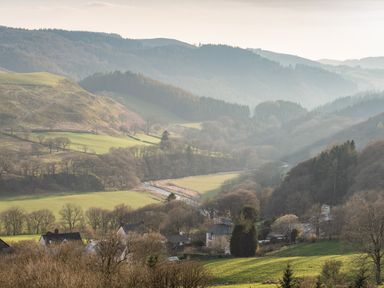 A rural village with houses near a river surrounded by hills and trees at Haka Lodge in Devil's Bridge