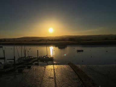 A sunset over a body of water with boats docked at a pier and hills in the background at Upham View in Woodbury