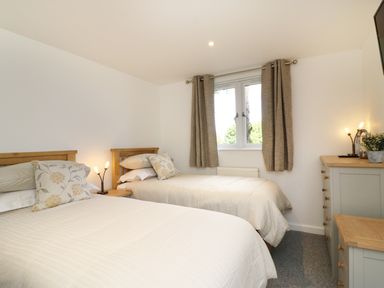 A bedroom with two single beds a window with curtains a chest of drawers and a small table with lamps at Upham View in Woodbury