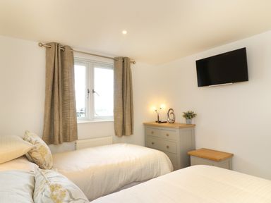 A bedroom with two single beds a dresser a small table a wall-mounted television and a window with curtains at Upham View in Woodbury