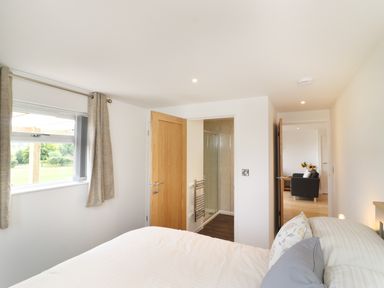 A bedroom with a bed and pillows near a window with curtains and two wooden doors leading to a bathroom and a living room at Upham View in Woodbury