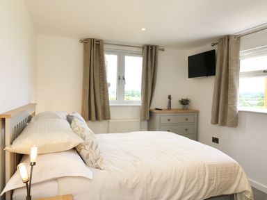 A bedroom with a bed a dresser pillows curtains and a wall mounted television at Upham View in Woodbury