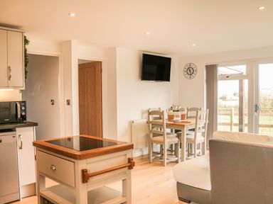 An open kitchen and dining area with a small island, dining table with chairs, wall clock, and TV at Upham View in Woodbury