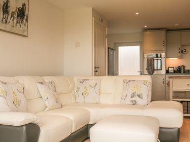 A living room with a white sectional sofa with floral cushions and a matching ottoman next to a kitchen area at Upham View in Woodbury