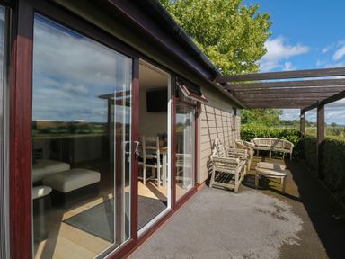 A patio with wooden chairs and a table outside a building with glass sliding doors at Upham View in Woodbury
