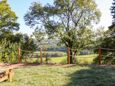 A garden area with grass a wooden bench trees and a rope fence overlooking fields at Little Silver Fox in High Bickington