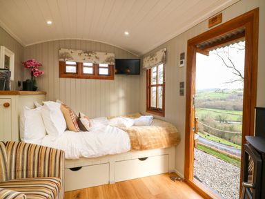 A bedroom with a bed a striped chair a wall mounted tv and an open door showing a countryside view at Little Silver Fox in High Bickington