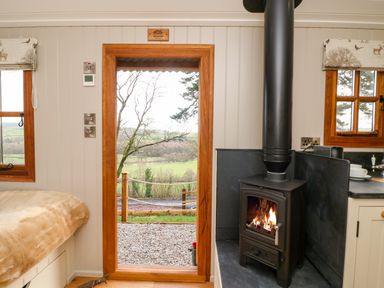 A room with a wood burning stove window with curtains and a door opening to a landscape at Little Silver Fox in High Bickington