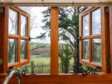 Open wooden window with metal latches looking out to a green landscape and trees at Little Silver Fox in High Bickington