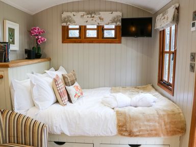A bedroom with a bed with pillows and a blanket a wall-mounted TV and windows with patterned blinds at Little Silver Fox in High Bickington