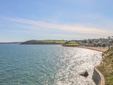 A coastal view with a beach houses on a hillside and a stone sea wall at Pugwash Cottage in Falmouth