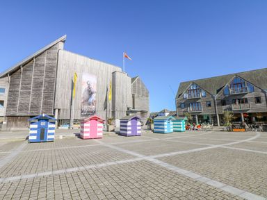 A plaza with colorful striped beach huts in front of a museum and adjacent multi-story wooden buildings with balconies at Pugwash Cottage in Falmouth