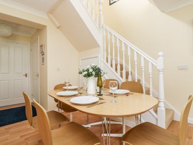 A dining area with a wooden table set for four near a staircase at Pugwash Cottage in Falmouth
