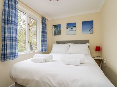 A bedroom with a double bed white linens three framed pictures blue plaid curtains and a small bedside table with a red lamp at Pugwash Cottage in Falmouth