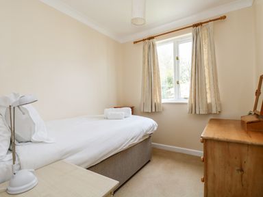 A bedroom with a single bed white bedding wooden dresser and bedside table with lamp at Pugwash Cottage in Falmouth