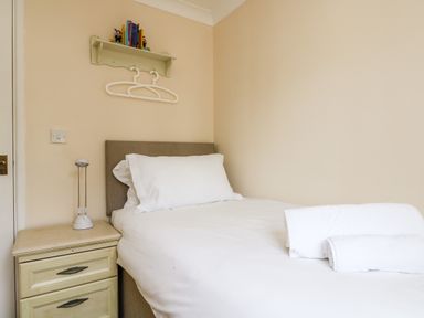 A bedroom with a single bed with white bedding and towels on it a bedside table with a lamp and a wall shelf with books Pugwash Cottage in Falmouth
