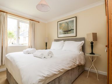 A bedroom with a double bed white bedding rolled towels bedside tables with lamps and a window at Pugwash Cottage in Falmouth