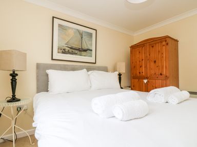 A bedroom with a bed with white linens and pillows with rolled towels on top two lamps on side tables and a wooden wardrobe at Pugwash Cottage in Falmouth