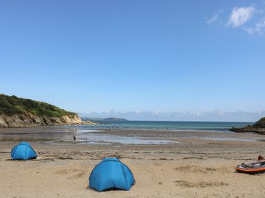 A beach with two blue tents and people walking near the shore at Pugwash Cottage in Falmouth