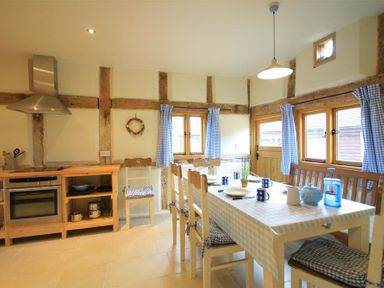A kitchen with wooden furniture and blue checkered curtains at Whites Farm Barn in Ledbury