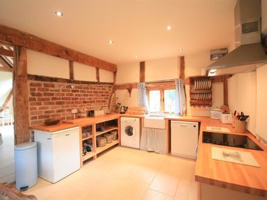 A kitchen with wooden countertops appliances and a window with curtains at Whites Farm Barn in Ledbury