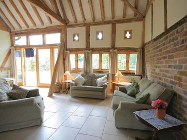 A living room with three sofas wooden beams exposed brick wall and windows with curtains at Whites Farm Barn in Ledbury