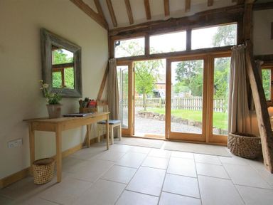 A room with a wooden table, chair, mirror on the wall, large glass doors opening to a garden at Whites Farm Barn in Ledbury