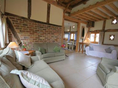A living room with sofas, armchairs, a brick wall, wooden beams, and a view into a dining area at Whites Farm Barn in Ledbury
