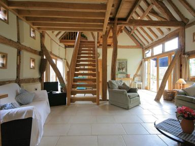 A living room with wooden beams a staircase armchairs and windows at Whites Farm Barn in Ledbury