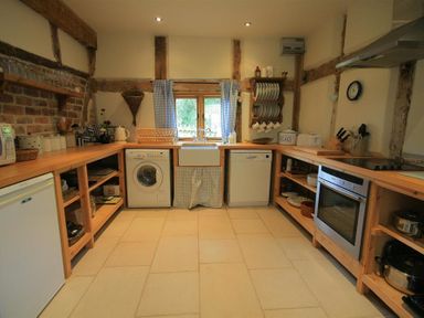 A kitchen with wooden countertops washing machine dishwasher oven and open shelves at Whites Farm Barn Ledbury