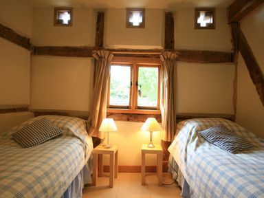 A bedroom with two single beds a window between them and two bedside tables each with a lamp at Whites Farm Barn Ledbury