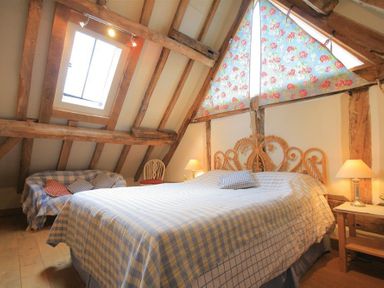 A bedroom with wooden beams a bed with checkered bedding a small sofa with pillows and a side table with lamps at Whites Farm Barn in Ledbury