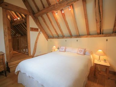 A bedroom with a double bed table lamps wooden beams and wooden flooring at Whites Farm Barn in Ledbury