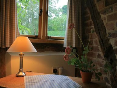 A wooden table with a lamp and a flower pot under a window with curtains at Whites Farm Barn in Ledbury