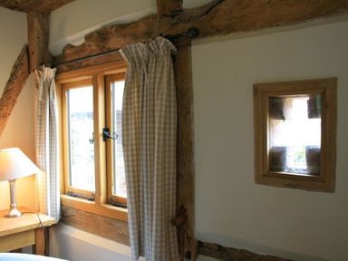 A window with checkered curtains and a lamp on a wooden table in a room at Whites Farm Barn in Ledbury