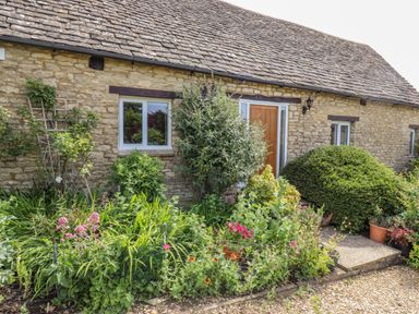 A stone cottage exterior with a garden and plants at Pheasant Cottage in Minster Lovell