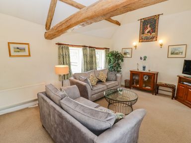 A sitting room with two grey sofas a glass coffee table wooden furniture and exposed wooden beams at Pheasant Cottage in Minster Lovell