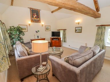A living room with two sofas a glass coffee table a lamp and wooden beams at Pheasant Cottage in Minster Lovell