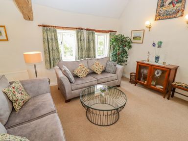 A living room with two sofas a glass coffee table a wooden cabinet and a potted plant at Pheasant Cottage in Minster Lovell