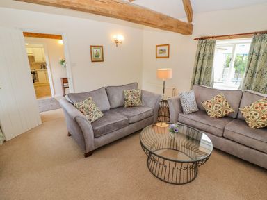 A living room with two grey sofas a glass coffee table and floral curtains at Pheasant Cottage in Minster Lovell