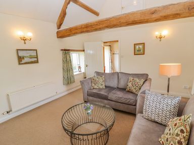 A living room with two sofas a round glass coffee table wooden beams on the ceiling and wall lights at Pheasant Cottage in Minster Lovell