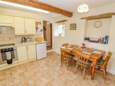 A kitchen with wooden dining table and chairs and cream cabinets at Pheasant Cottage in Minster Lovell