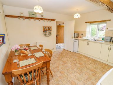 A kitchen with wooden dining table set with placemats plates and glasses beside white cabinets and a window at Pheasant Cottage in Minster Lovell