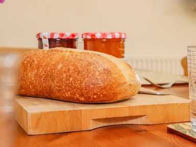 A loaf of bread on a wooden cutting board with jars of jam in the background at Pheasant Cottage in Minster Lovell