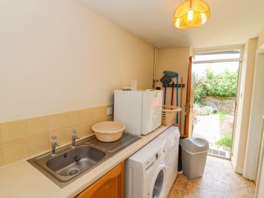 A laundry room with a washing machine sink and cleaning tools near an open door leading outside at Pheasant Cottage in Minster Lovell